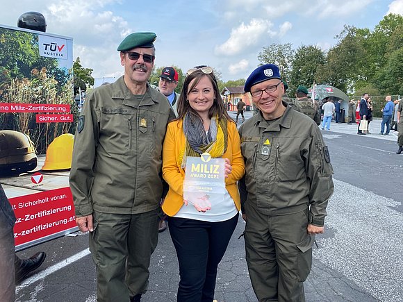 Eine Dame hält den Miliz Award 2021 in den Händen. Links und rechts von ihr je ein uniformierter Mann.